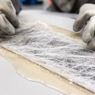 Detalle de resina y fibra durante el laminado manual sobre una mesa de trabajo limpia